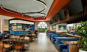 Ravintola, jossa on pöytiä, tuoleja ja sinisiä sohvia sekä baari taustalla. (Tekoälyn luoma teksti)