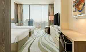 Hotellihuone, jossa on kaksi sänkyä, työpöytä, tuoli ja televisio. Ikkuna näkymällä yli kaupungin. (Tekoälyn luoma teksti)