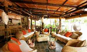 Trooppisesti sisustettu istuinryhmä rottinkikalusteilla ja oransseilla tyynyillä. (Tekoälyn luoma teksti)