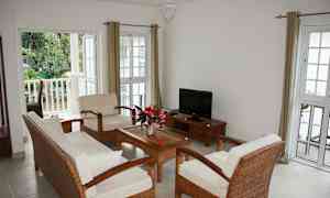 Vaalea olohuone, jossa on istuimet neljälle hengelle, sohvapöytä ja televisio. (Tekoälyn luoma teksti)