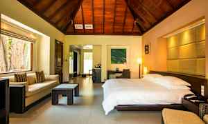 Hotellihuone, jossa on suuri sänky, sohva ja pöytä, puupaneeli katossa. (Tekoälyn luoma teksti)