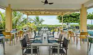 Ulkoterassi, jossa on pöytiä ja tuoleja vehreyden keskellä ja näkymä merelle. (Tekoälyn luoma teksti)