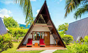 A-muotoinen puutalo, jonka edessä on kaksi aurinkotuolia, ympärillä vehreyttä. (Tekoälyn luoma teksti)