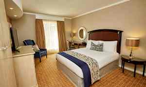 Hotellihuone, jossa on pedattu sänky, nojatuoli, työpöytä ja pyöreä peili seinällä. (Tekoälyn luoma teksti)