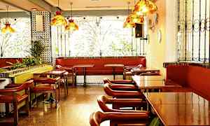 Ravintola, jossa on pöytiä, tuoleja ja penkkejä ikkunoiden koristeltujen rautaristikoiden vieressä. (Tekoälyn luoma teksti)