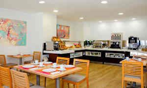 Ruokailutila, jossa pöydät ovat katettuina ja buffet sisältää kahviautomaatin ja aamiaistarjottavia. (Tekoälyn luoma teksti)