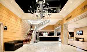 Hotellin aula, jossa on marmorilattia ja tyylikäs kattokruunu. Portaikko johtaa aulasta ylös, ja vastaanotto on näkyvissä. (Tekoälyn luoma teksti)