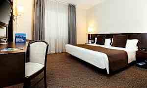 Hotellihuone, jossa on parivuode, kirjoituspöytä, tuoli ja suuret ikkunat verhoilla. (Tekoälyn luoma teksti)