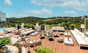 Kuva terassista, jossa on valkoisia kalusteita ja näkymä vehreään maisemaan kirkkaan sinisen taivaan alla. (Tekoälyn luoma teksti)