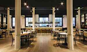 Tyylikäs ravintola, jossa on pöytiä ja tuoleja sekä hyvin valaistu baaritiski taustalla. (Tekoälyn luoma teksti)