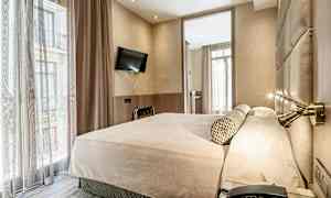 Hotellihuone, jossa on iso sänky, seinälle asennettu televisio ja suuret ikkunat verhoilla. (Tekoälyn luoma teksti)