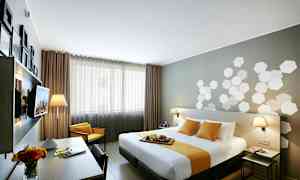 Moderni hotellihuone, jossa on parivuode valkoisilla ja keltaisilla tekstiileillä. Huoneessa on kirjoituspöytä, maljakko ja pöytävalaisimia. (Tekoälyn luoma teksti)