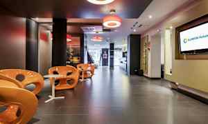 Nykyaikainen hotelliaula, jossa on oransseja tuoleja ja pieniä valkoisia pöytiä. (Tekoälyn luoma teksti)