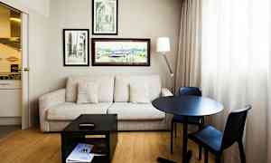 Huone, jossa sohva, pöytä ja kaksi tuolia, seinäkoristeet ja pieni keittiö. (Tekoälyn luoma teksti)