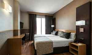 Hotellihuone, jossa on kaksi vierekkäin olevat yhden hengen vuodetta, työpöytä ja tuoli sekä seinälle kiinnitetty TV. (Tekoälyn luoma teksti)