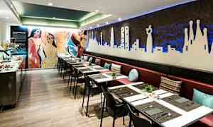 Ravintola, jossa on pitkä penkki ja pöytiä liinoilla sekä seinäkoristeita. (Tekoälyn luoma teksti)