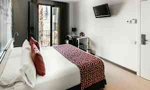 Moderni hotellihuone, jossa on suuri sänky, parvekkeen ovet ja työpöytäalue. (Tekoälyn luoma teksti)