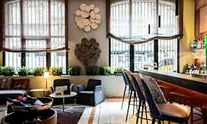 Sisäkuva, joka esittää oleskelutilaa tai baarialuetta, jossa on tuoleja, pöytä, baaritiski ja koristeellisia elementtejä seinillä. (Tekoälyn luoma teksti)