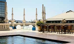 Kattoterassi, jossa on pylväitä, moderneja huonekaluja ja matala vesiallas. (Tekoälyn luoma teksti)