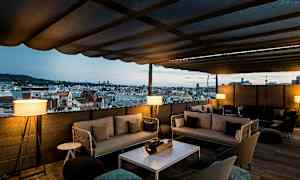 Kattoterassi, jolta on näkymä kaupungin horisonttiin. Terassilla on sohvia ja pöytiä. (Tekoälyn luoma teksti)
