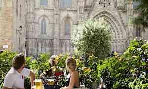 Ihmiset istuvat pöydän ääressä, ympärillä on vehreyttä, ja taustalla näkyy upea rakennus. (Tekoälyn luoma teksti)