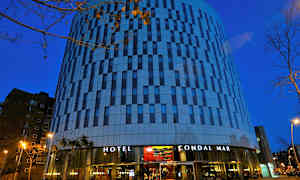 Hotelli, jossa on moderni arkkitehtuuri ja julkisivu, jossa on lasia ja betonia, kuvattuna hämärässä. (Tekoälyn luoma teksti)