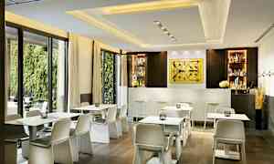 Moderni kahvila, jossa on valkoisia pöytiä ja tuoleja baarin edessä kirkkaassa sisustuksessa. (Tekoälyn luoma teksti)