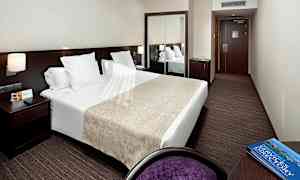 Hotellihuone, jossa on parivuode, yöpöytä lampulla, peili ja kirjoituspöydän tuoli. (Tekoälyn luoma teksti)