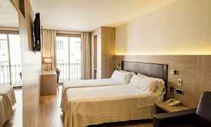 Hotellihuone, jossa on kaksi erillistä sänkyä, kirjoituspöytä ja tuoli suuren ikkunan edessä, jossa on parvekekaide. Seinälle on asennettu televisio. (Tekoälyn luoma teksti)