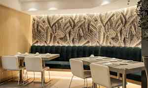 Ravintolasisustus, jossa pöytiä ja tuoleja lehväkuvioisen seinän edessä. (Tekoälyn luoma teksti)