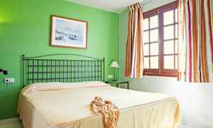 Makuuhuone, jossa on vihreä seinä, beige päiväpeite, musta sängynpääty ja ikkuna, jossa on raidalliset verhot. (Tekoälyn luoma teksti)