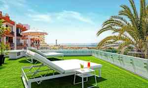 Kattoterassi, jossa on nurmi, aurinkotuoleja, pieni pöytä juomien kanssa ja näkymä ympäristöön. (Tekoälyn luoma teksti)