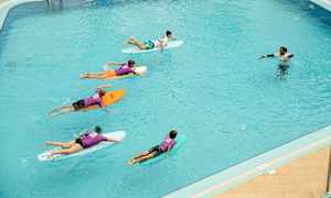 Ryhmä ihmisiä makaa surffilaudoilla altaassa, ja ohjaaja seisoo vedessä. (Tekoälyn luoma teksti)