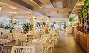 Ravintolan sisätila, jossa puuelementtejä, valkoiset huonekalut ja vihreitä kasveja. (Tekoälyn luoma teksti)