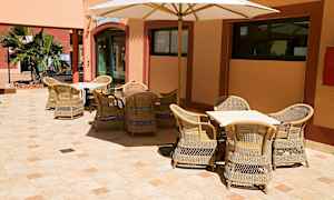 Ulkotarjoilualue, jossa on rottinkikalusteita ja päivänvarjo, sijaitsee kivetetyllä pihalla. (Tekoälyn luoma teksti)