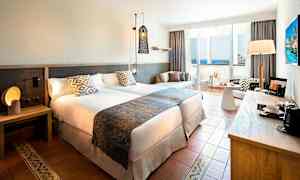 Hotellihuone, jossa kaksi sänkyä, yöpöytä, istuinryhmä ja parveke merinäköalalla. (Tekoälyn luoma teksti)