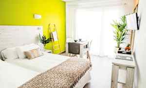 Valoisa ja moderni makuuhuone, jossa vihreä tehosteseinä, sänky valkoisin ja beigein vuodevaattein sekä pöytä ja tuolit suuren ikkunan lähellä. (Tekoälyn luoma teksti)