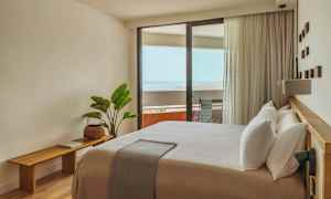 Valoisa ja modernisti sisustettu hotellihuone, jossa on suuri sänky ja parveke merinäköalalla. (Tekoälyn luoma teksti)