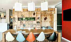 Huone, jossa on suuri puinen pöytä ja värikkäitä tuoleja, ympärillä puuhyllyt täynnä kirjoja ja koristeita. (Tekoälyn luoma teksti)