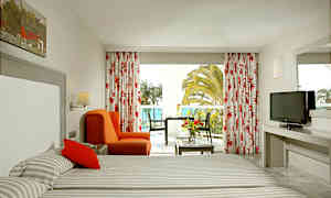 Hotellihuone, jossa kaksi sänkyä, punainen tuoli, pöytä ja parveke näkymällä. (Tekoälyn luoma teksti)