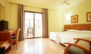 Valoisa hotellihuone, jossa kaksi sänkyä, työpöytä, tuoli ja parveke lasiovilla. (Tekoälyn luoma teksti)