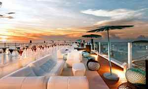 Kattoterassi merinäköalalla auringonlaskun aikaan, modernilla sisustuksella, johon kuuluu sohvia, varjostimia ja pöytiä. (Tekoälyn luoma teksti)