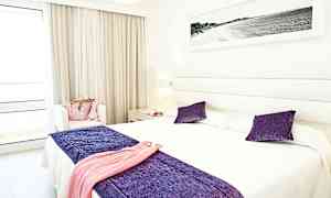 Vaalea hotellihuone, jossa on parivuode ja koristeita violettina ja valkoisena. (Tekoälyn luoma teksti)