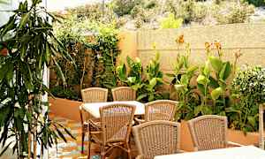 Ulkokalusteet rottinkisilla pöydillä ja tuoleilla vehreän puutarhan edessä. (Tekoälyn luoma teksti)