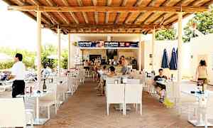 Ulkoalue, jossa on baari, pöytiä ja tuoleja katon alla. Ihmiset istuvat pöydissä ja tilaavat baarista. (Tekoälyn luoma teksti)