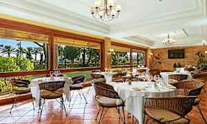 Tyylikäs ravintola, jossa on katetut pöydät ja punottuja tuoleja. Suuret ikkunat tarjoavat näkymän puutarhaan. (Tekoälyn luoma teksti)