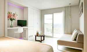 Valoisa hotellihuone, jossa on sänky, sohva, pöytä ja parveke merelle päin. (Tekoälyn luoma teksti)