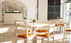 Vaaleat puukalusteet, joissa on oranssi istuinpehmuste, valoisassa huoneessa suurilla ikkunoilla. (Tekoälyn luoma teksti)