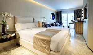 Moderni hotellihuone, jossa on iso sänky, sohvaryhmä ja minibaari suuren ikkunan edessä. (Tekoälyn luoma teksti)