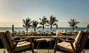 Kaksi nojatuolia ja pöytä terassilla, josta näkymä palmupuihin, varjoihin ja merelle. (Tekoälyn luoma teksti)